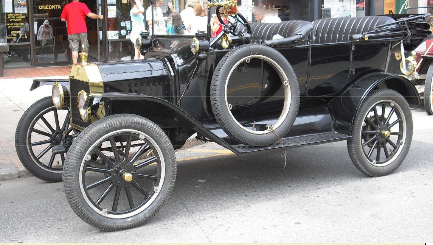 Early Ford touring automobile showing spare tires, split rims, and period construction.