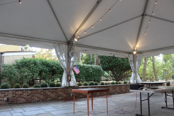 Outdoor meeting space at Liberty Hall Museum with tables, string lights, and an American flag under a large white tent.