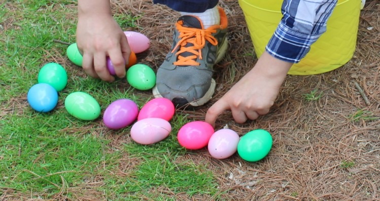 A child picking up colorful plastic Easter eggs from the grass