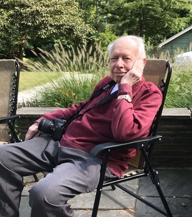 Bill Frolich, longtime UCHS Treasurer, seated outdoors with a camera