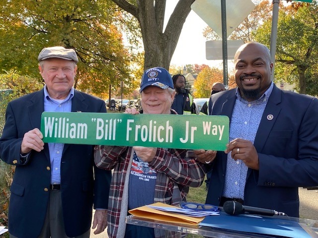 Dignitaries holding a green street sign reading “William ‘Bill’ Frolich Jr Way.”