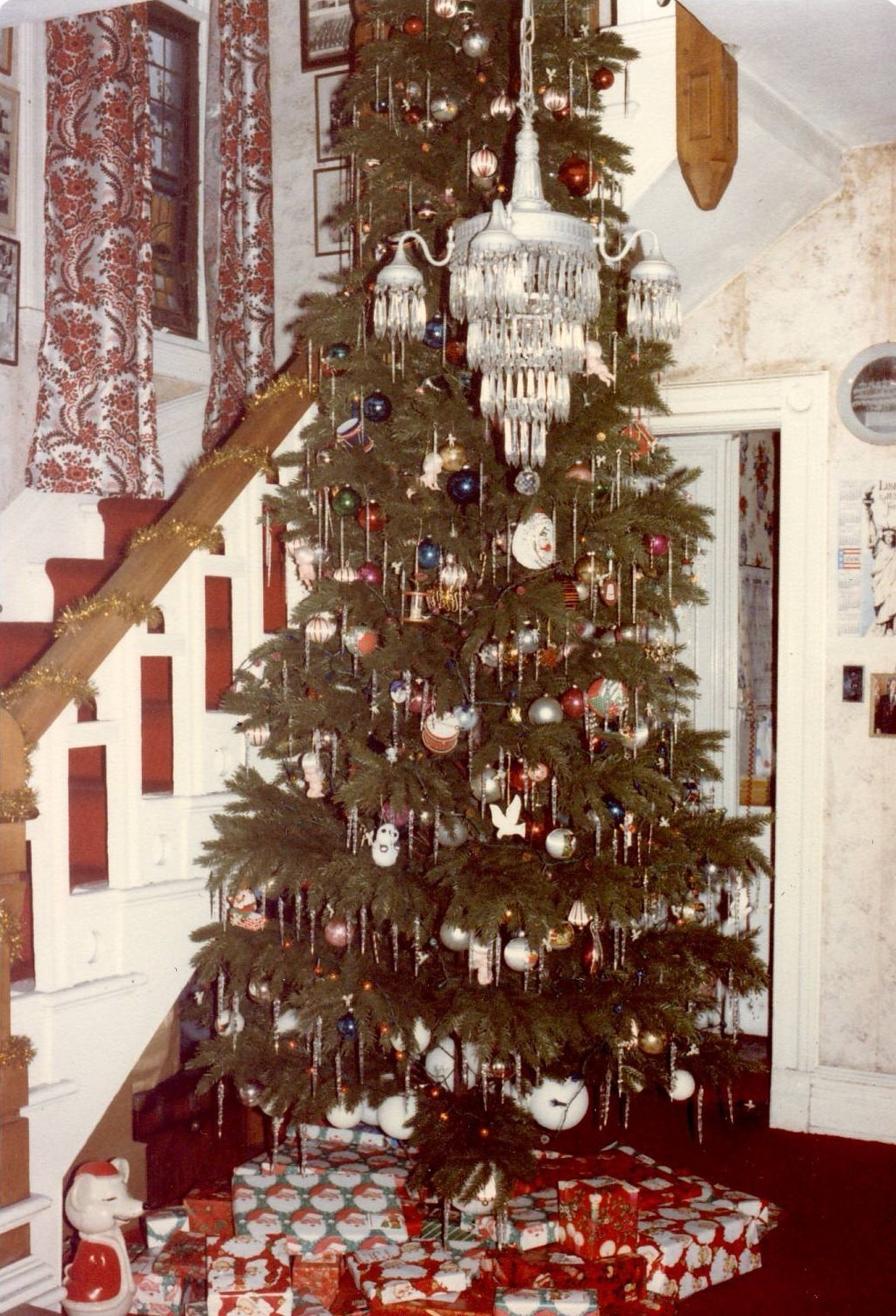 Tall Christmas tree decorated with ornaments and tinsel with wrapped gifts beneath it in a vintage home interior